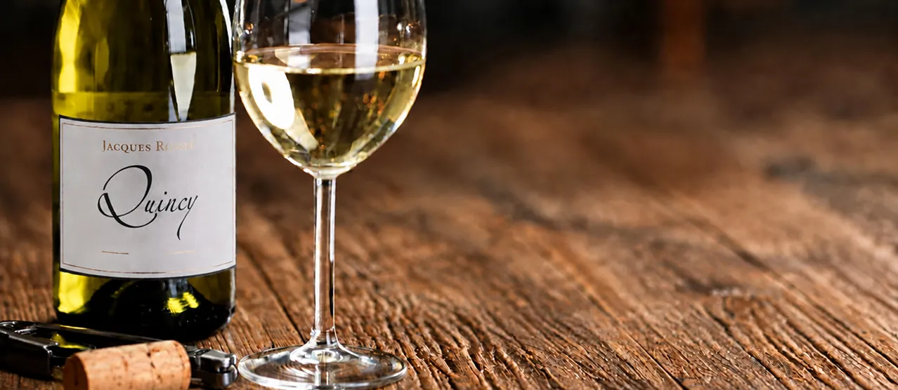 Bouteille de Quincy Jacques Rouzé et verre de vin blanc sur une table en bois